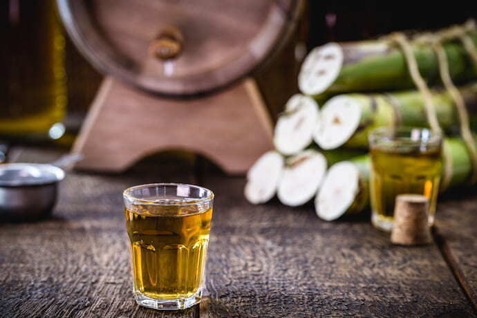 Copo de shot com cachaça e pedaços de cana ao fundo