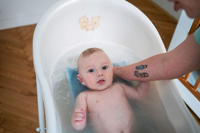 Bebê sendo segurado pelo pai em banheira com almofada para banho azul