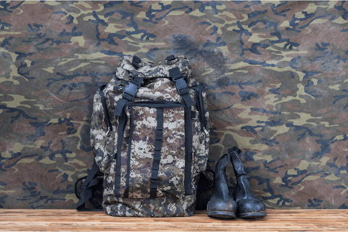 Mochila militar e botas em fundo com estampa militar