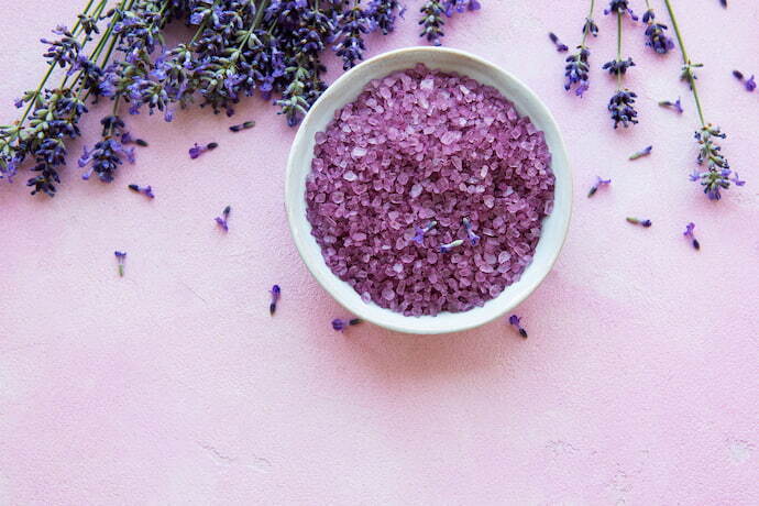 Recipiente com sais de banho roxos e alguns galhos de lavanda