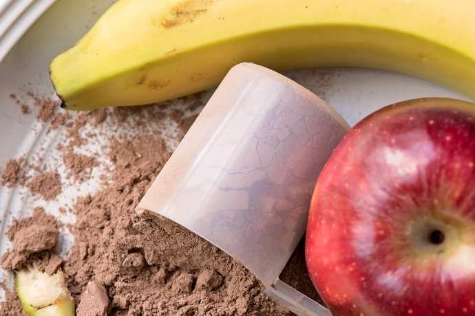 Pó preparatório de shake para emagrecer de chocolate ao lado de frutas