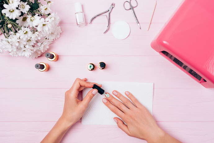 Mulher passando base para crescer a unha com vários itens de manicure ao redor.