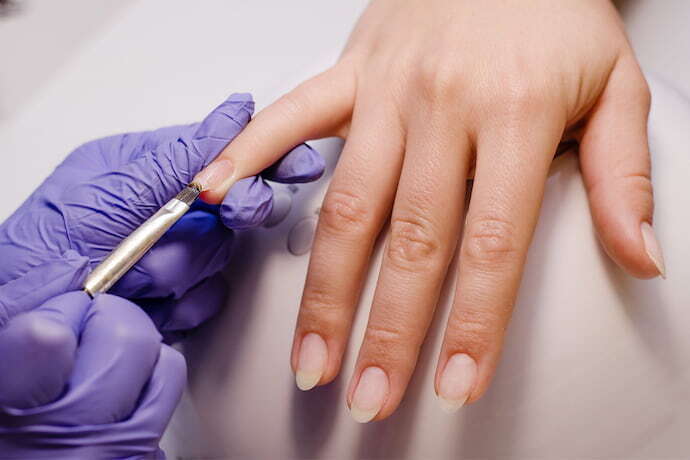 Manicure com luva passando base para crescer unha em cliente.