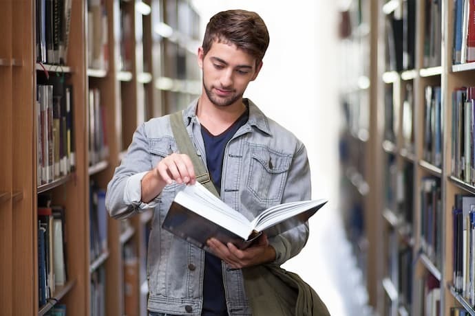 Homem em biblioteca lendo livro de mitologia nórdica.