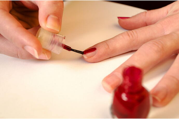 Mulher pintando a própria unha de vermelho.