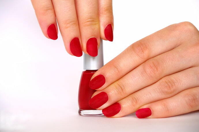 Mulher com unhas pintadas de vermelho segurando embalagem de esmalte