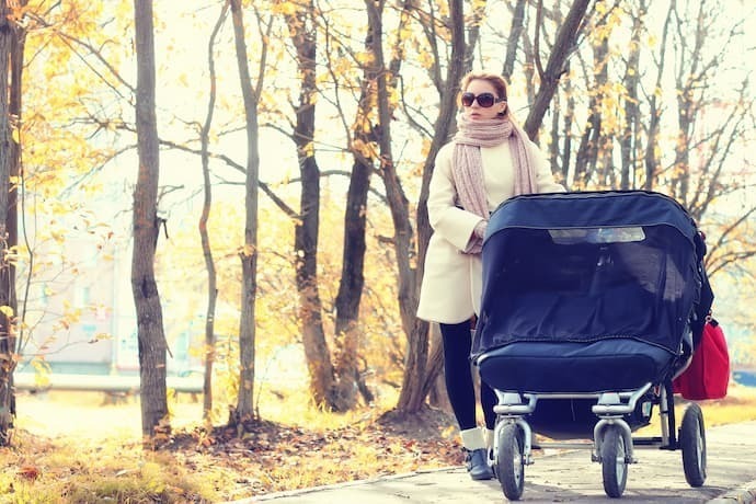 Mãe empurrando carrinho de bebê para gêmeos