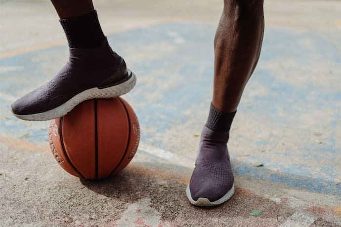 Homem apoiando bola de basquete com pé.