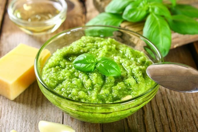 Molho pesto em recipiente de vidro e ingredientes em volta