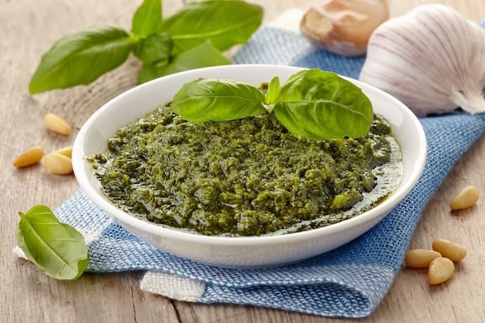 Molho pesto dentro de prato branco em cima de mesa de madeira com ingredientes ao lado