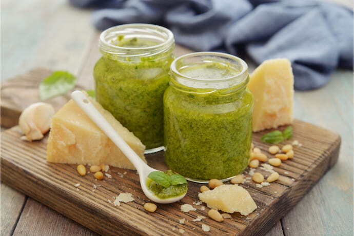 Molho pesto em recipiente de vidro e ingredientes em volta