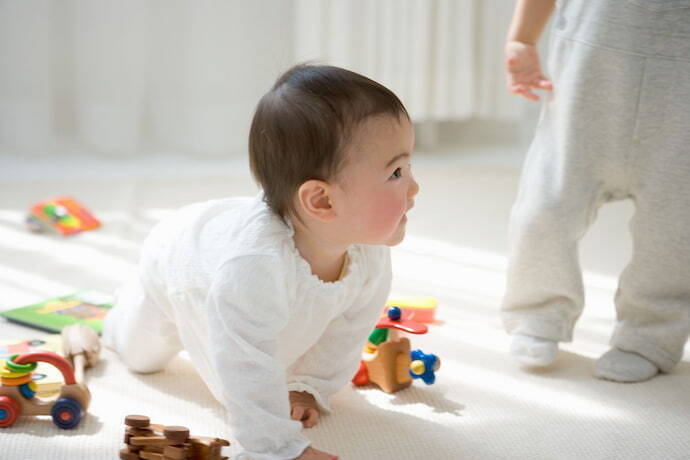 Bebê engatinhando ao lado de brinquedos.