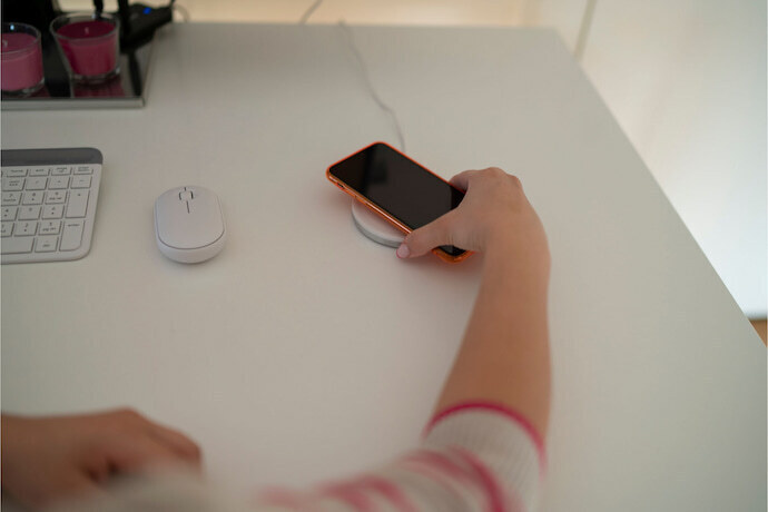 Pessoa colocando Iphone para carregar em carregador sem fio para Iphone redondo branco em cima de mesa.