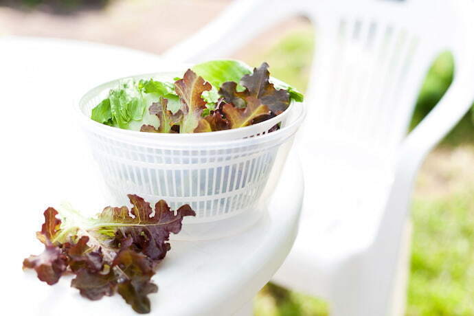 Secador de salada branco em cima de mesa branca.