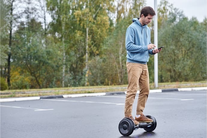 Homem andando em hoverboard preto mexendo em celular.