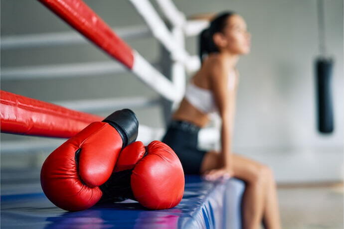 Mulher sentada em ringue com luva de boxe ao lado.