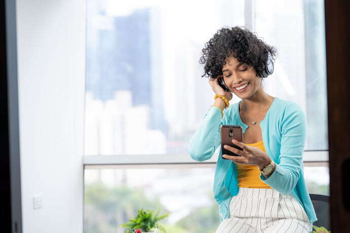 Mulher feliz com headphone Bluetooth e celular na mão.