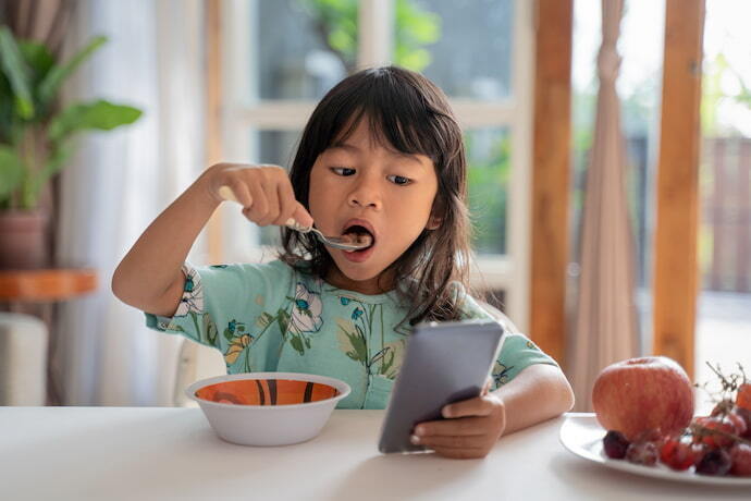 Menina comendo e usando celular