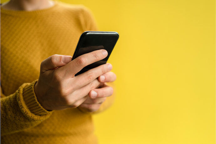 Mulher segurando celular em fundo amarelo