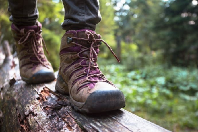 Indivíduo com botas de trilha andando em um tronco 