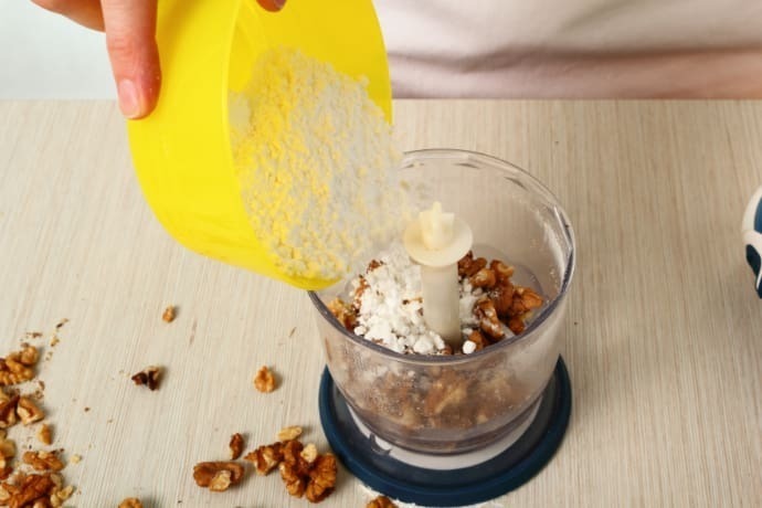 Indivíduo com processador fazendo bolo com avelã em uma mesa.