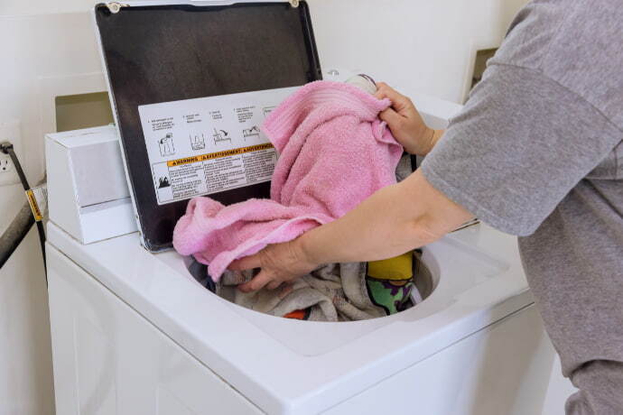 Indivíduo de camiseta cinza lavando roupa no tanquinho.