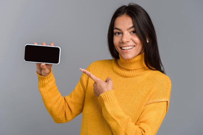 Mulher indicando com a mão para o celular em um fundo cinza