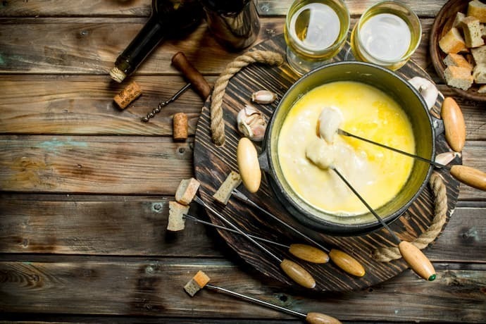 Delicioso queijo fondue com azeitonas e vinho branco sobre uma tábua de madeira.