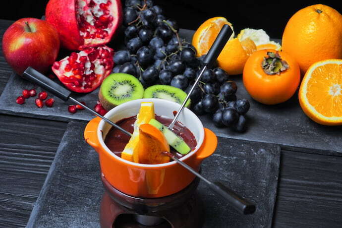 Fondue laranja e cheia de chocolate e recipientes com frutas.