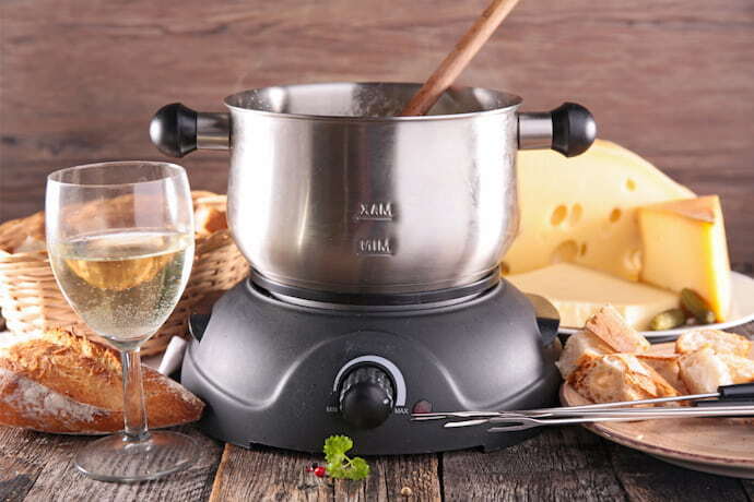 Aparelho de fondue Elétrico de aço inox com ingredientes ao redor.