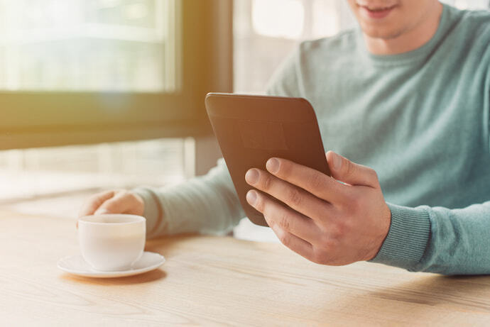 Um homem lendo no seu e-reader acompanhado de uma xícara de café 