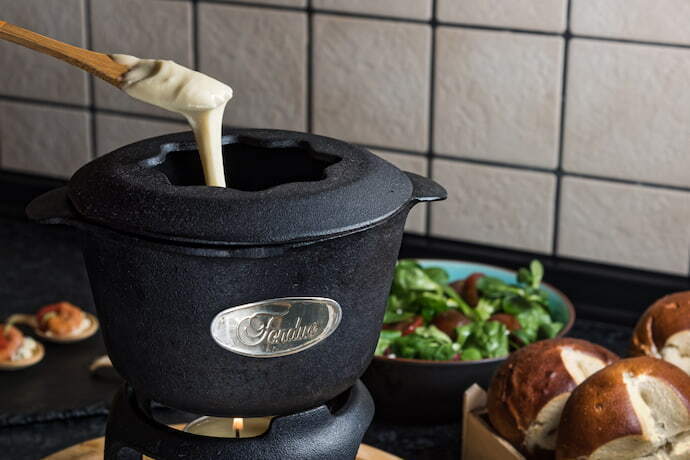 Fondue de ferro cheia de queijo, sobre uma mesa na cozinha.