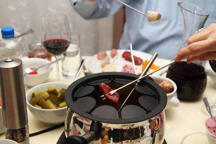 Close-up de um fondue de carne e outros ingredientes ao redor.