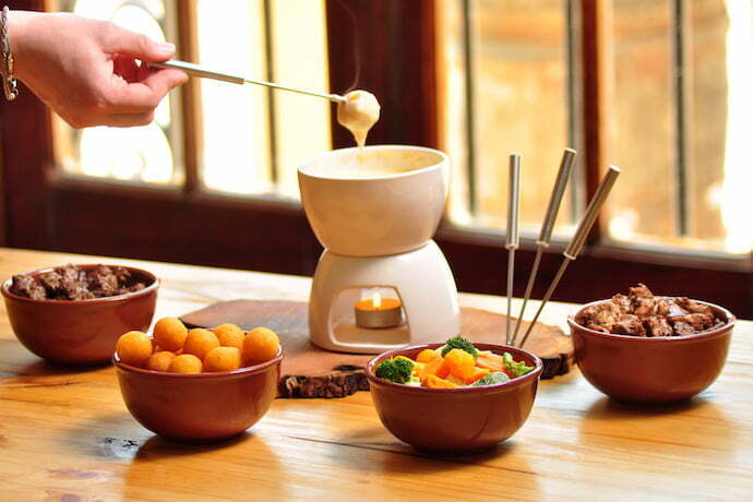 Fondue de queijo sobre uma mesa e com ingredientes ao redor.