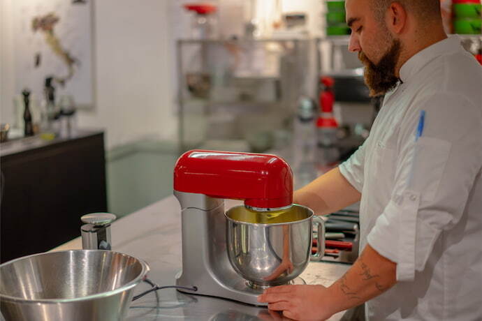 Homem usando uma batedeira de cor vermelha em uma cozinha industrial.