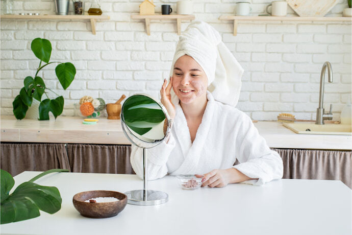 Mulher feliz aplicando esfoliante facial no rosto na cozinha de sua casa.