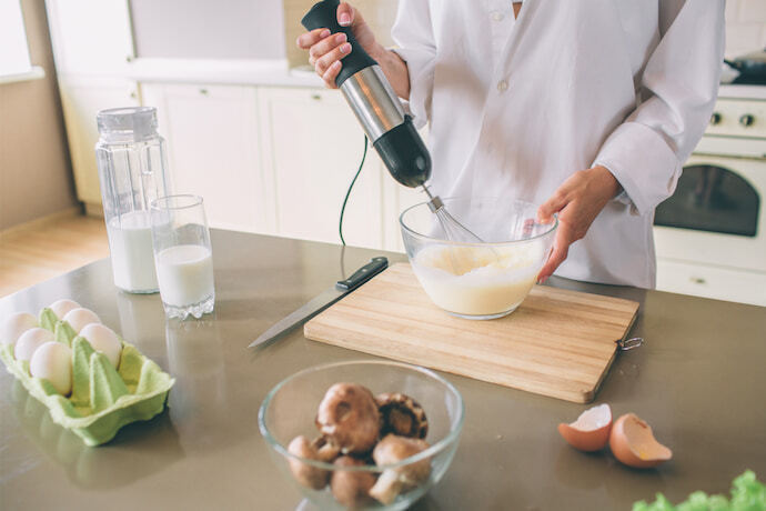 Mulher misturando ovos e leite com um mixer de mão. 