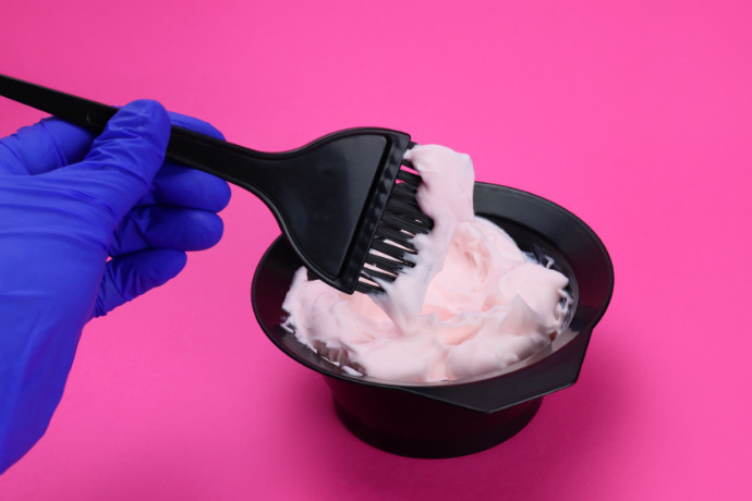 Indivíduo preparando a tintura de cabelo em um fundo rosa