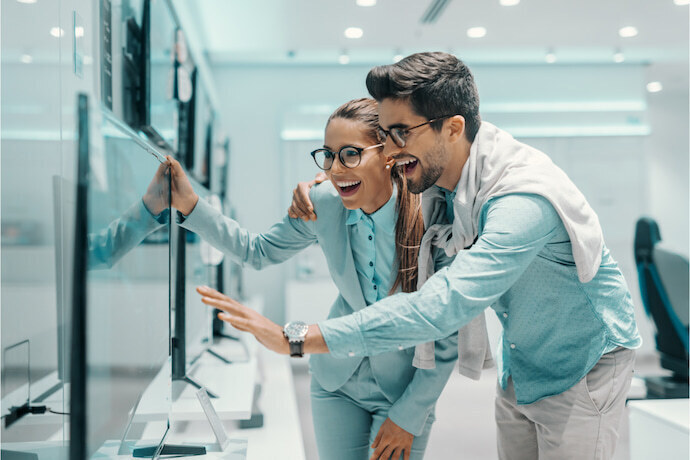 Casal feliz, escolhendo uma Smart TV na loja de eletrônicos.