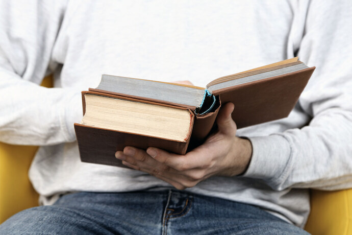 Homem sentado, segurando dois livros e lendo um deles.