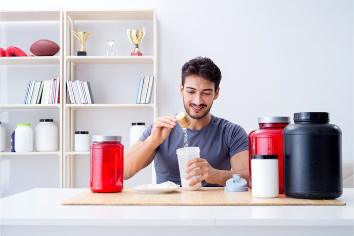 Homem sentado e preparando whey protein sobre a mesa.