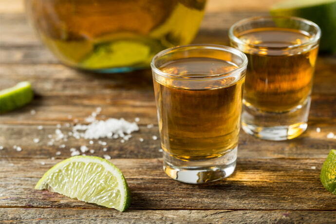 Dois shots de tequila reposado em uma superfície de madeira.