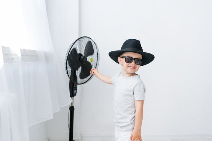 Criança feliz perto do ventilador de coluna 