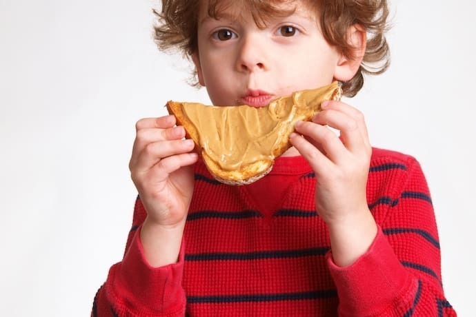 Menino comendo pão com pasta de amendoim