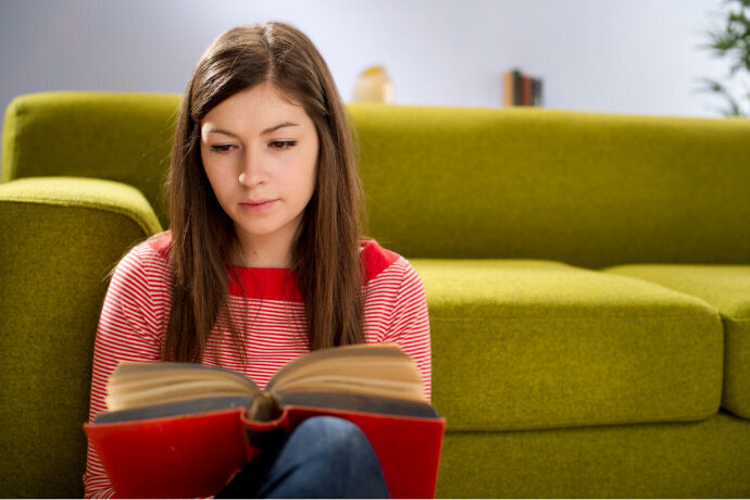 Mulher lendo um livro encostada no sofá