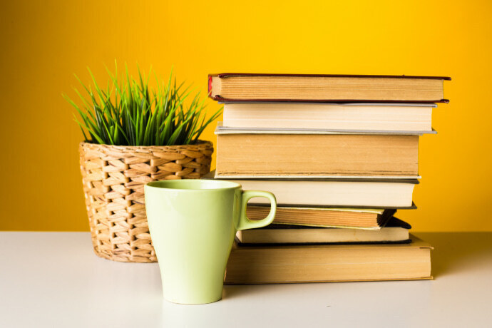 Uma pilha de livros, um vaso e uma xícara sobre a mesa