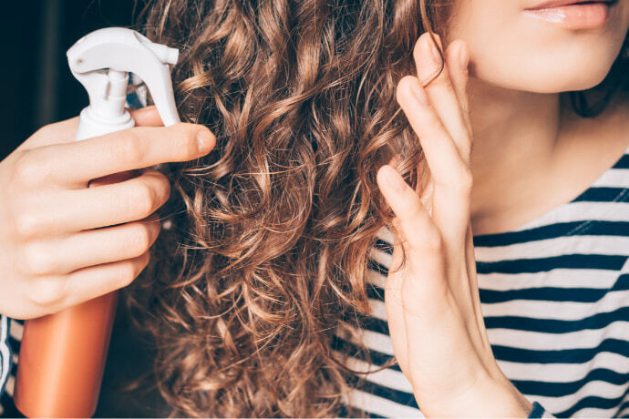 Mulher usando um spray no cabelo cacheado