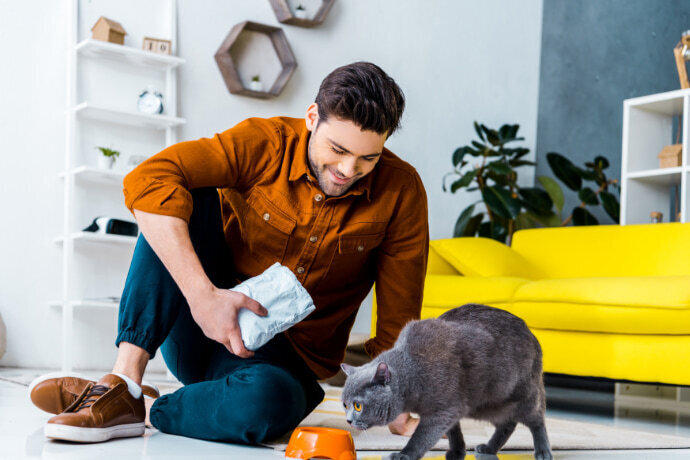 Homem sorridente segurando um pacote de petiscos e observando o gato