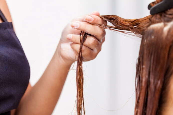 Uma mulher aplicando creme no cabelo da outra