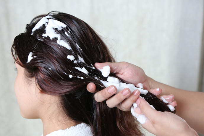 Mãos aplicando creme no cabelo do cliente